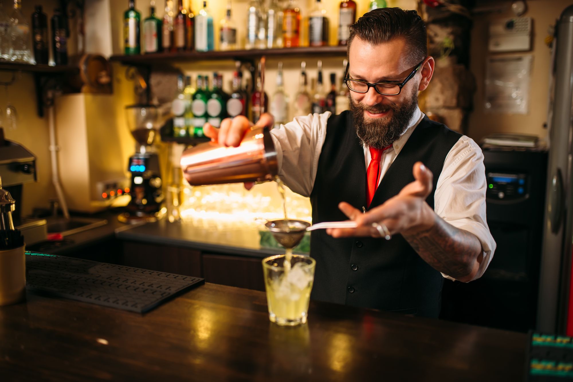 Barman flaring behind bar counter. Restaurant shelves with alcoholic drinks bottles on background