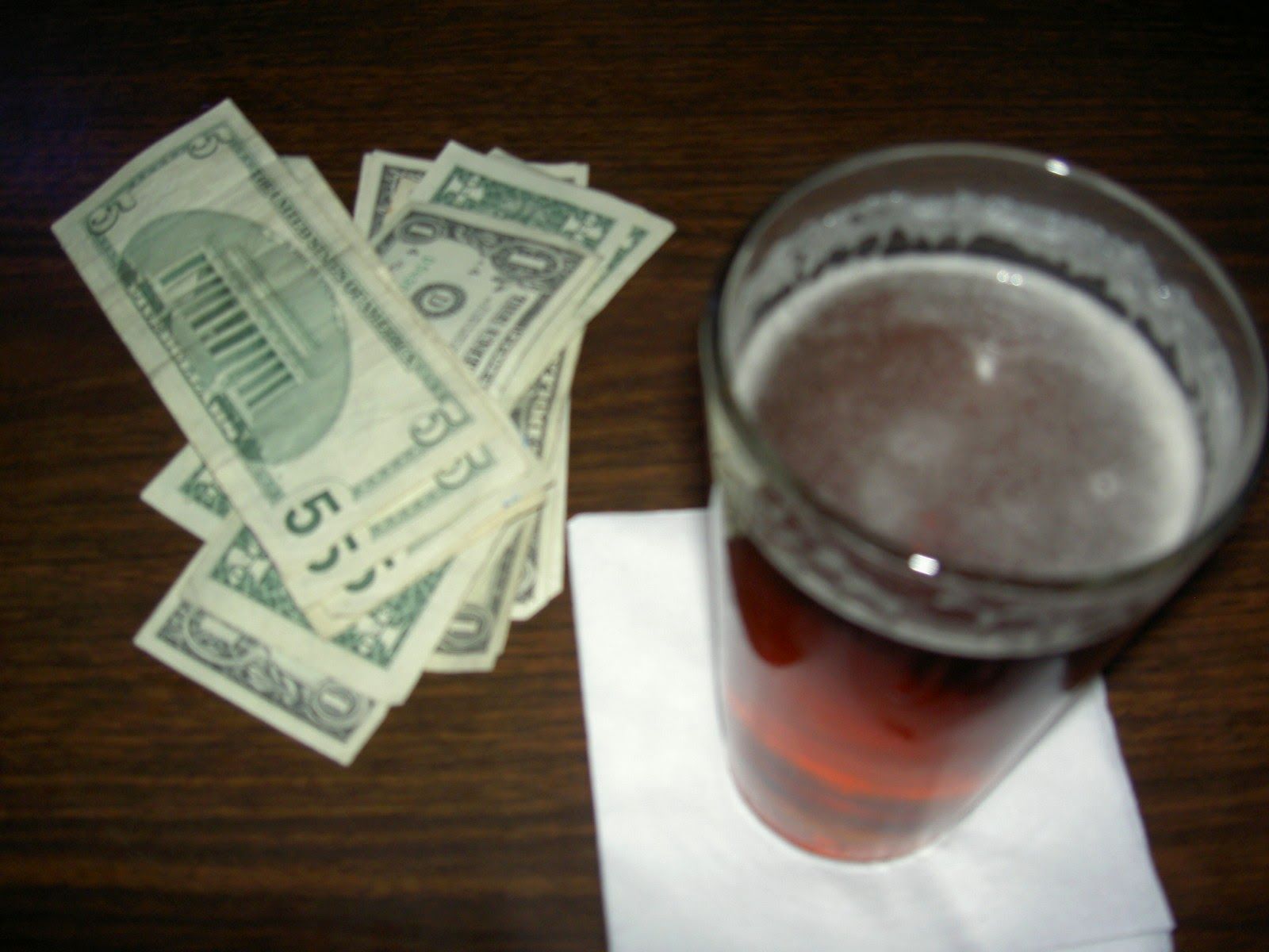 A full lager beer and cash on a bar.