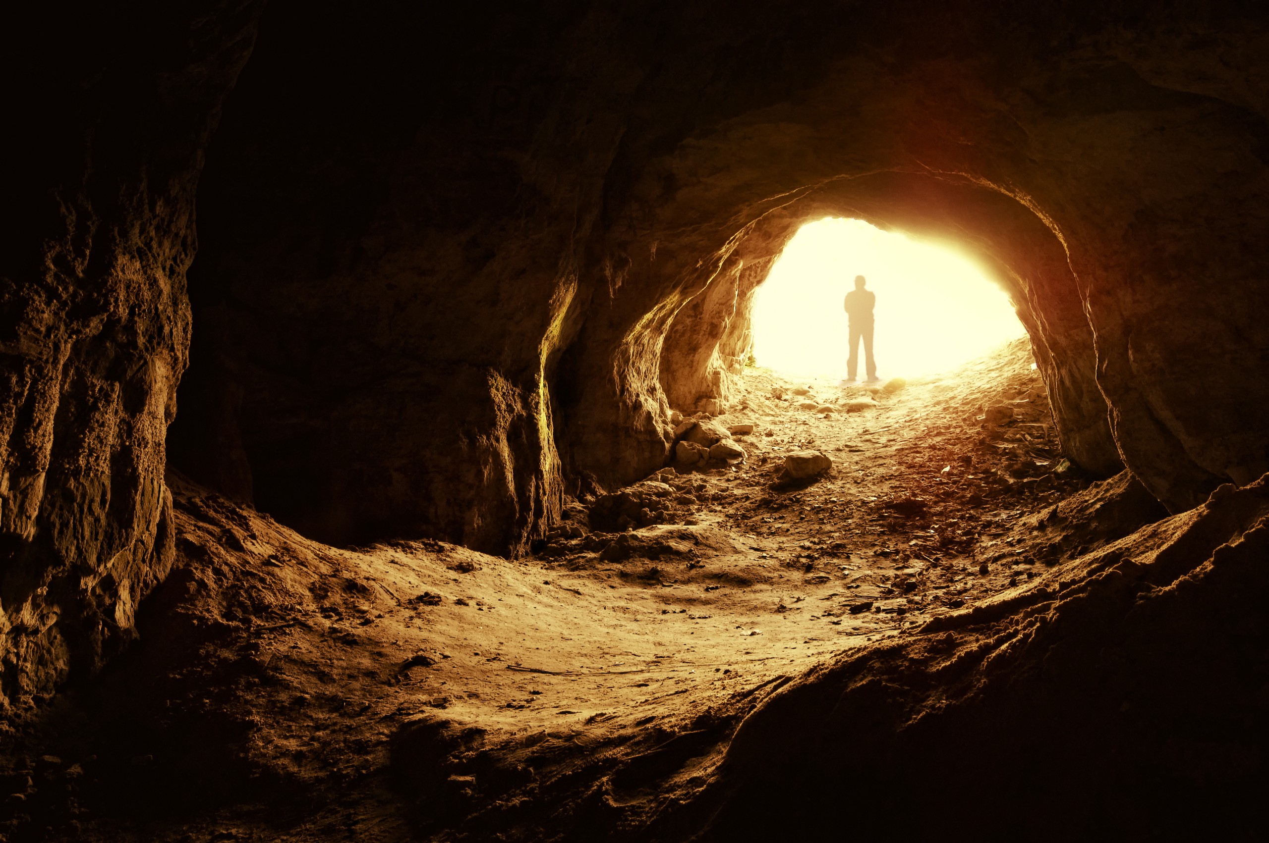 A person standing in front of a cave entrance.