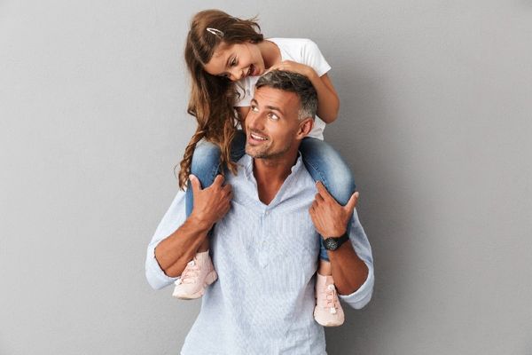 Daughter smiling and sitting on the neck of her father over gray background