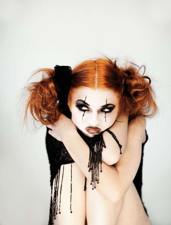 Woman with white-faced Halloween make up and red hair poses in front of white background